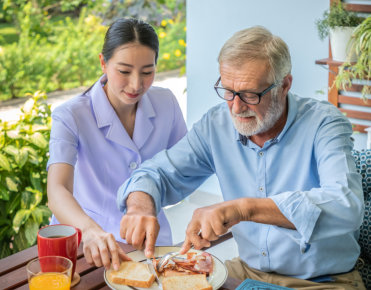 caregiver watching senior man eat breakfast