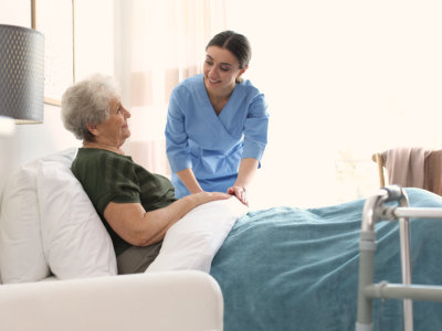 caregiver holding the hand of senior woman lying in bed